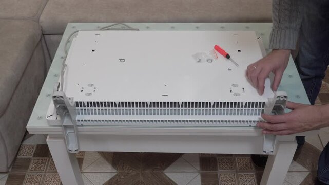 assemble an electric heater in the room, a man assembles an electric convector at home, heating in the cold season