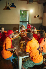 Group of football fans, men and women, sitting at table at bar and clinking glasses in moment of celebration victory of favorite team. Concept of friendship, soccer fan, championship, support. Ad