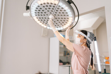 Female doctor wearing medical uniform adjusting light preparation performing operation at hospital. Surgeon adjusting surgical lamp before medical procedure. Concept of professional health treatment.