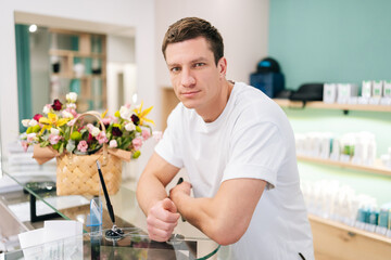 Portrait of confident muscular male client standing waiting at counter of modern dentistry clinic, looking at camera. Front view of confident young man customer in shopping mall