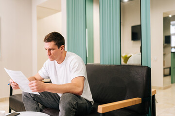 Fototapeta premium Thoughtful male client reading contract for real estate property purchase. Thoughtful man reading terms of conditions of document, making decision about house purchase or financial investment