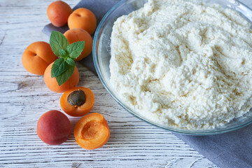 A bowl of dough and fresh apricots on a white wooden background. Preparation of apricot pie.