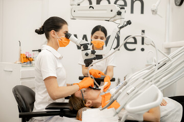 female dentist and an assistant treat the teeth of a young female patient. A dentist with an assistant at work in a dental office.