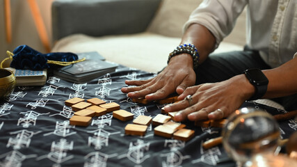 Close up hands arranging wooden runes on a table covered with a mystical cloth. Forecasting and...