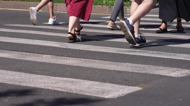 People walking on the street.  Pedestrians crossing a city street. Person's foot crossing crosswalk intersection, car traffic. Summer time. Crowd crossing  zebra in city town.