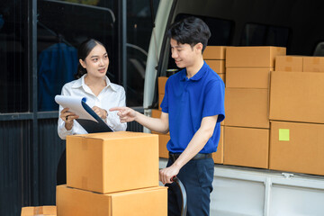 Signing for the package. Smiling young delivery man holding a cardboard box, woman putting...