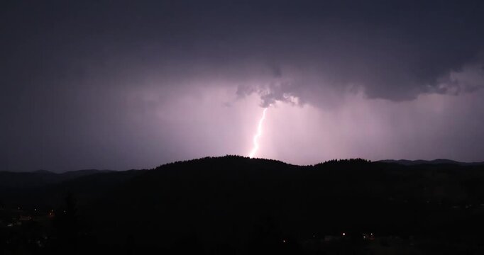 Lightning storm in the night sky at mountain. Multiple lightnings and thunders illuminate night sky and hills with firs