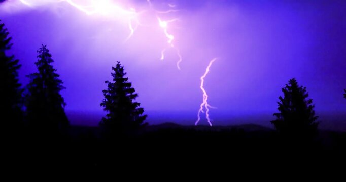 Lightning storm in the night sky at mountain. Multiple lightnings and thunders illuminate night sky and hills with firs