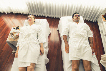 Fototapeta premium Caucasian couple customer enjoying relaxing anti-stress spa massage and pampering with beauty skin recreation leisure in day light ambient salon spa at luxury resort or hotel. Quiescent