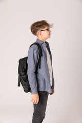 Fototapeta premium Side view teenager boy in grey shirt with school bag on white background. Back to school, education concept. Copy space
