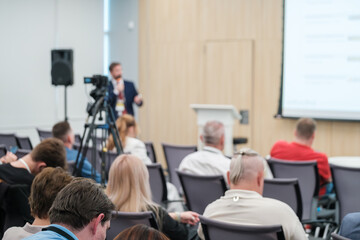 Business conference presentation with speaker, audience, and video camera recording session