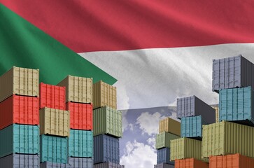 Sudan flag and big stack of shipping cargo containers in docks with sky background close up