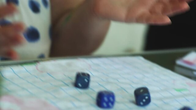 A woman playing a Yahtzee game throwing dice on a table closeup and writing the score