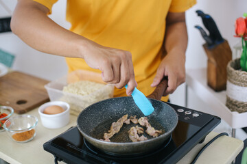 Man Hands With Tongs Touches Sliced Meat That Frying In Fry Pan On Electric Stove
