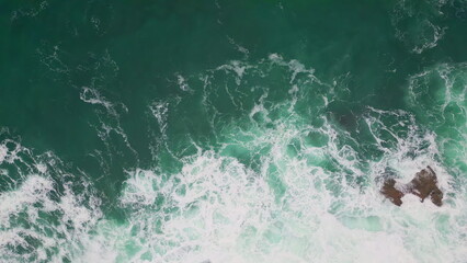 Sea washing rocky shore top view. Azure waves foaming splashing rough cliffs