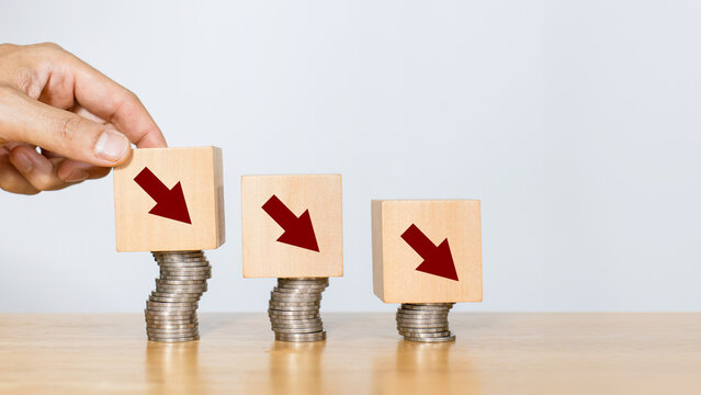Cost, economy recession and cost reduction concept. Hand putting wooden block with arrow down sign indicate economy recession or decreasing expense to maximize profits