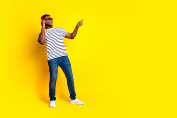 Fototapeta premium Full body portrait of nice young man headphones point finger empty space wear t-shirt isolated on vibrant yellow color background