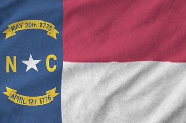 Fototapeta premium North Carolina US state flag depicted on folded wavy fabric of old cloth close up