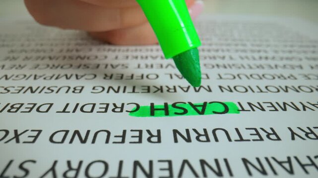 Close up shot of woman hand working with document, green marker in female hand marked highlighted a word cash in text.
