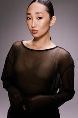 Asian woman in sheer top posing in front of gray background fashionable and elegant look