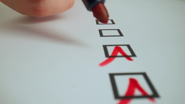Close up shot of woman hand working with document, red marker in female hand writing check marks in row of text boxes in document.