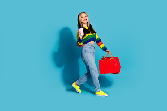 Full body photo of attractive young woman shopping bags walk drink coffee dressed stylish striped clothes isolated on blue color background