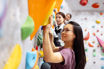 A group of multiracial women doing rock climbing in the gym.