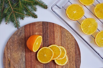 Slicing Orange on a wooden board for further drying on a baking sheet in the oven, for decoration.