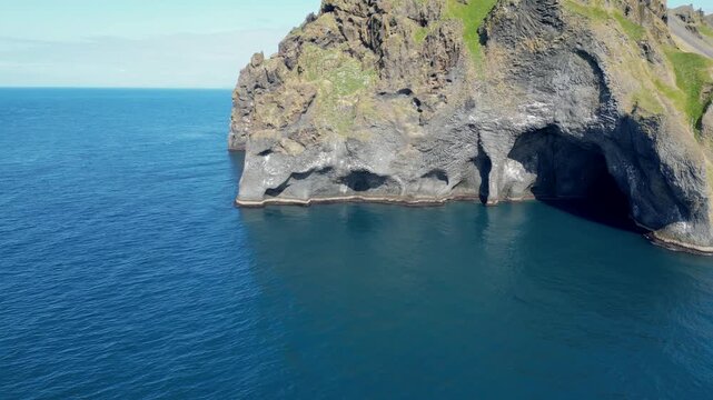 A drone image of Elephant Rock in Iceland. The striking basalt formation resembles an elephant's head dipping into the deep blue ocean, with clear skies adding to the stunning natural beauty. 4K