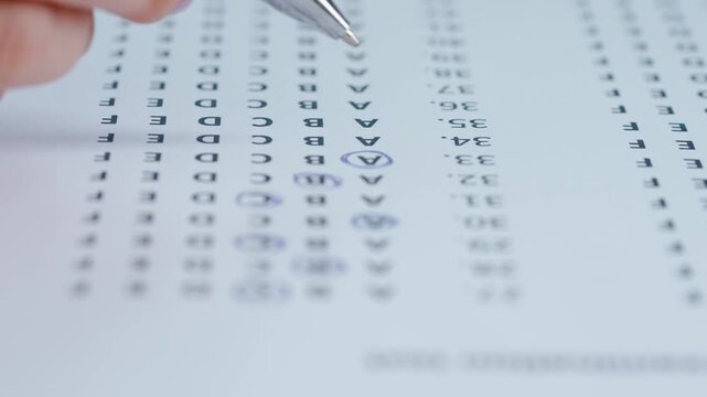 Close up shot of woman at the desk working with important exam document, student reading and circling letters answers in test with pen.