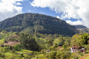 Beautiful landscape in the Andes Mountains. Jardin, Jardín, Antioquia. Blue sky, white clouds;  farmhouses, green lush vegetation, crops and fields.