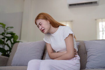 Young Woman Experiencing Stomachache While Sitting on Couch in Living Room, Expressing Pain and Discomfort