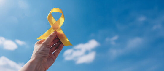 Close-up of a hand holding a yellow ribbon against a blue sky symbolizing support, awareness, and Suicide Prevention Day