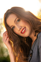 Close up portrait of a beautiful smiling young woman, with her long brown hair back lit by the late afternoon sunlight. 