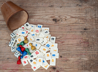 Classic board games, leather cup with dice and rummikub tiles on wooden background