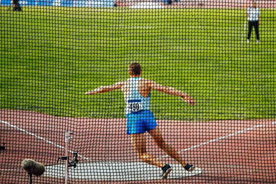 discus throw, male athlete makes an attempt, view through grid - Powered by Adobe