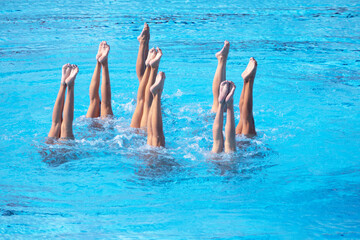 Artistic female swimming team performing synchronized legs movement in swimming pool