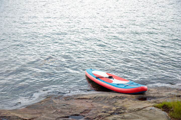 Paddle surf board and oar or SUP board in water on the stony shore in Finland, Baltic Sea, Gulf of Finland
