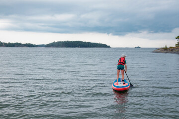 Little boy paddling on a paddle surfboard sup board in Baltic sea, Gulf of Finland, kids vacation, summer holidays in Finland