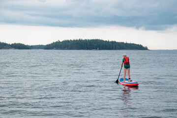 Naklejka premium Little boy paddling on a paddle surfboard sup board in Baltic sea, Gulf of Finland, kids vacation, summer holidays in Finland