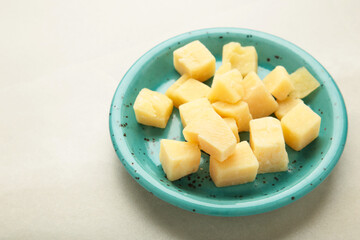 Cheese cubes on blue plate on light background. Parmesan