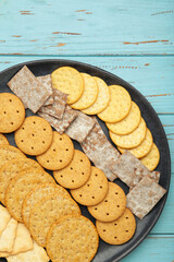 Different crackers on plate on blue wooden background. Vertical photo