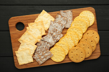 Different crackers on cutting board on black wooden background