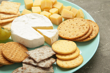 Different types of cheese with crackers on mint plate.