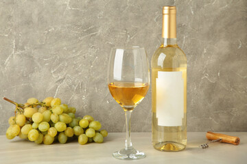 Bottle and glass with white wine with grape on grey background.