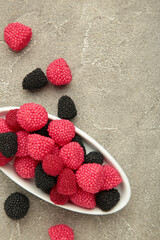 Raspberry and blackberry candy on plate on grey background. Vertical photo