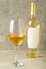 Unlabeled bottled of white wine with half empty wineglass standing on grey background. Vertical photo
