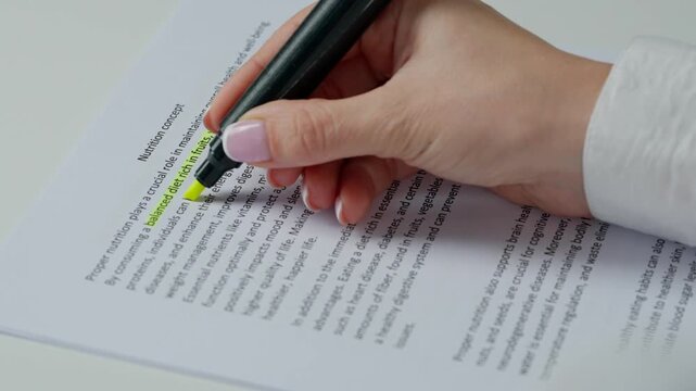 Close up shot of woman at the desk working with document, reading and highlighting important parts in text with yellow marker in hand.