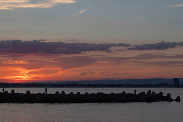 silhouettes of people on the breakwater at sunset