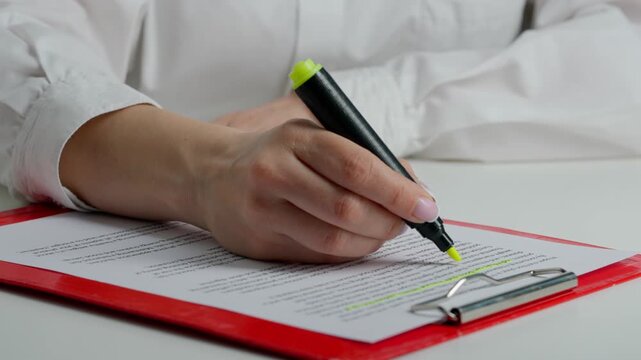 Close up shot of woman at the desk working with document, reading and highlighting important parts in text with yellow marker in hand.